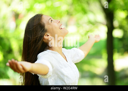 Attraktive junge Frau im Frühjahr oder Sommer Garten seitlich stehend, die Arme ausgestreckt und erfreuen Sie Ihren Kopf in den Himmel genießen die Frische und die Schönheit der Natur angehoben Stockfoto