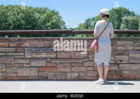 Von hinten gesehen, reife weibliche Betrachtung der Landschaft von der Brücke. Stockfoto