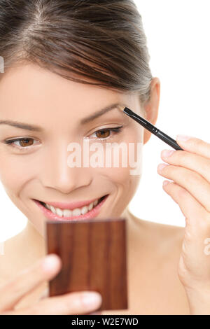 Make-up Girl putting Augenbraue Farbe in Pocket Mirror suchen. Lächelnd glückliche junge Schönheit Frau Anwendung Make-up mit Eye Brow brush Holding Pocket Mirror isoliert weißer Hintergrund. Asiatische kaukasische Mädchen Stockfoto