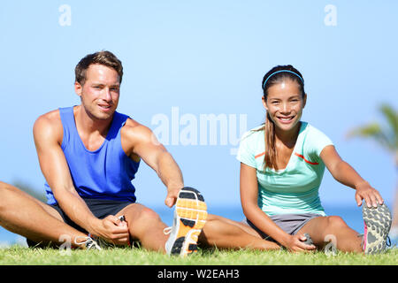 Dehnungsübungen - Fitness Paar außerhalb tun erstreckt. Passen Mann und Frau tun Kniesehne leg stretching Training im Sommer. Schöne gemischtrassiges Paar. Stockfoto