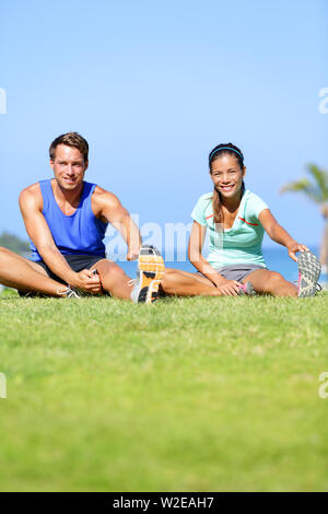 Fitness - paar Dehnübungen im Freien. Passen Mann und Frau tun Kniesehne bein Übung dehnen und strecken Training im Freien im Sommer. Schöne gemischtrassiges Paar. Stockfoto