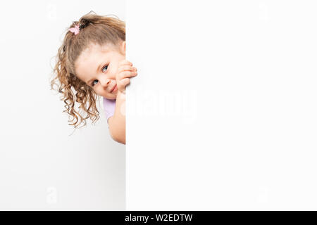 Lächelnd blue eyed kleines Mädchen spähen hinter einer weißen Tafel. Stockfoto