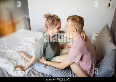 Glückliche junge zärtlich Paar sitzen einander gegenüber auf dem Bett und Kuscheln nach dem Ruhezustand Stockfoto