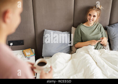 Glückliche Ehefrau mit Smartphone an ihren Ehemann mit Tasse Kaffee am Morgen suchen Stockfoto