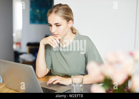 Junge weibliche Freiberufler in casualwear auf Laptop Display während Netzwerk zu Hause Stockfoto