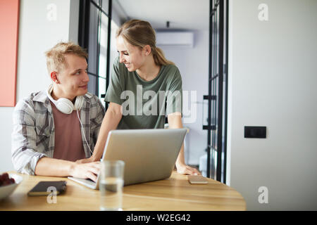 Junges Paar Interaktion von Tisch, während Menschen mit Kopfhörern Surfen im Netz Stockfoto