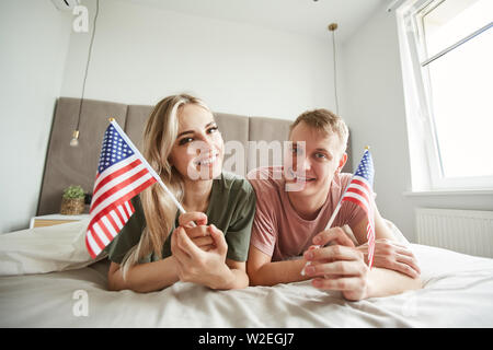 Junge fröhliche Patrioten mit amerikanischen Fahnen auf dem Bett liegend vor der Kamera und genießen Tag-off Stockfoto
