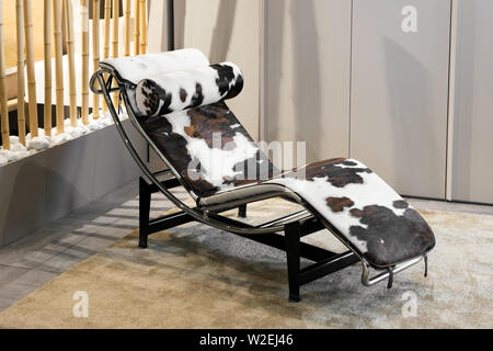 Elegante, moderne geschwungene Récamiere mit Tier auf einem Metallrahmen im Inneren auf eine Wolldecke in einem stilvollen Haus mit neutralen Beige Braun Dekor ausblenden Stockfoto