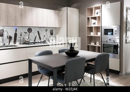 Moderne Küche mit künstlerischen Splash Back über einem weißen Zähler, in Schränke und Geräte und eine Zentrale, Tisch und Stühlen in einem stilvollen beige Bro gebaut Stockfoto