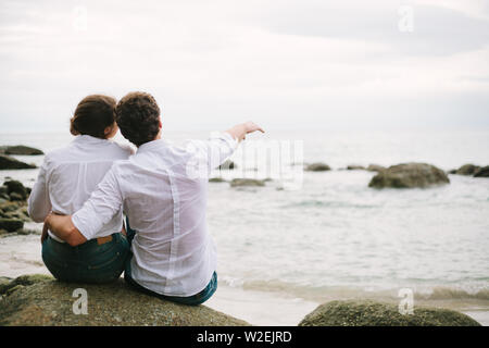 Ein Mann eine Frau zeigt mit der Hand in die Ferne. Sie sitzen und auf das Meer schauen. Zusammen Einsamkeit. Stockfoto