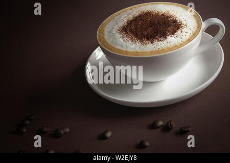 Tasse Cappuccino mit Sahne und Kaffee Bohnen auf braunem Hintergrund Stockfoto