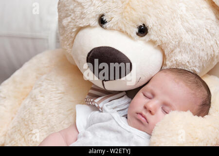 Friedliche Neugeborene schlafen mit riesigen Flauschigen Teddybär Stockfoto