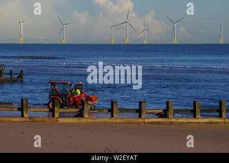 Traktor Abräumen Sturm Sand von Aberdeen Strandpromenade an einem sonnigen Wintertag. Offshore Wind Farm am Horizont. Schottland, Großbritannien. Stockfoto