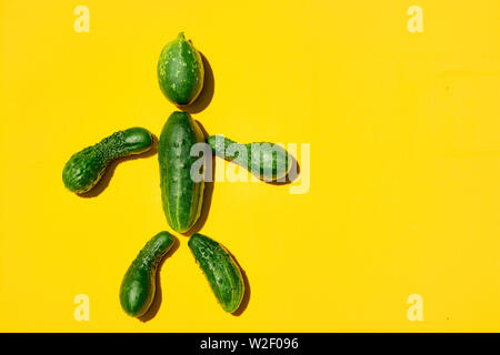 Gurke Mann auf einem gelben Hintergrund. Abbildung des Menschen von Gurken. Kopieren Sie Platz. Gurken für Designer. Ansicht von oben. Gurke Ernte. Landwirtschaft, Gard Stockfoto