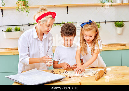 Mutter und seine Kinder bereiten aromatisiert Cookies in einem geräumigen Weißen Küche. Mama lehrt seine Kinder zu kochen. Gemeinsamen Zeitvertreib mit Familie. Stockfoto