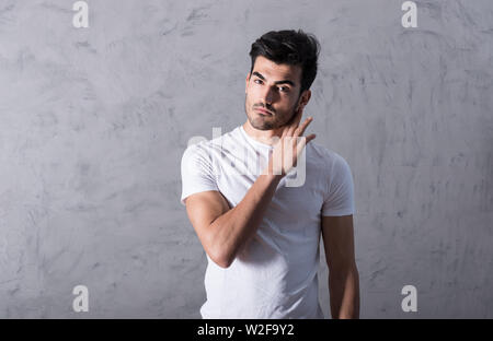 Ein hübscher junger Mann in einem weißen T-Shirt stand vor einer grauen Wand in einem Studio. Stockfoto