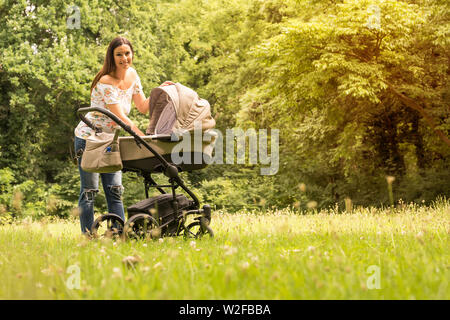 Eine schöne Mutter Kontrolle ihr Baby in einem Kinderwagen in den Park an einem sonnigen Tag. Stockfoto