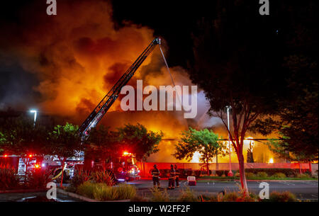 Modesto, CA, USA. 8. Juli, 2019. Eine von 5 Leiterwagen von Modesto Feuer und Ceres Feuerwehren schießt Wasser am nördlichen Ende der Struktur. Modesto Feuerwehr reagierte auf eine funktionierende Struktur Feuer an der Ecke von Tully Road und der 9th Street Dienstag, Juli 7, 2019 um 9:00 Uhr. Das Feuer ging schnell um mehrere Alarme bringen 3 Feuer Lkw zusammen mit mehreren anderen Motoren aus ganz Stanislaus County. Credit: Marty Bicek/ZUMA Draht/Alamy leben Nachrichten Stockfoto