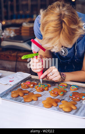 Nicht erkennbare Frauen Konditor Hand dekorieren ein gingerman mit einem Spritzbeutel, zeichnen ein Lächeln, die es süss, Spaß und lecker. Frau, die ging Stockfoto