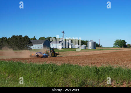 Traktor pflügen Feld mit Silos im Hintergrund Stockfoto