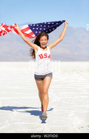 Sieger Athlet Frau läuft mit amerikanischer Flagge und USA T-Shirt. Runner girl Übersicht gewinnen Geste aufgeregt und glücklich im Freien in der Wüstenlandschaft. Freundliche fitness Frau Gewinner zujubeln, in voller Länge. Stockfoto
