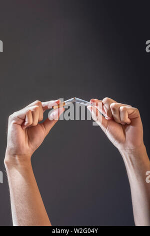 Hände brechen eine Zigarette auf schwarzem Hintergrund Stockfoto