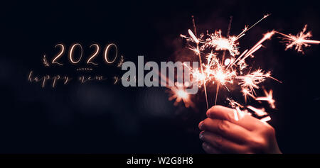 Frohes neues Jahr 2020 Text mit Hand, die brennende Wunderkerzen Feuerwerk Knall mit auf einem schwarzen bokeh Hintergrund in der Nacht, holiday Celebration Event party, d Stockfoto