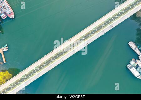 Lange schmale Brücke über einen großen Fluss mit Schiffen An der Küste angedockt Stockfoto