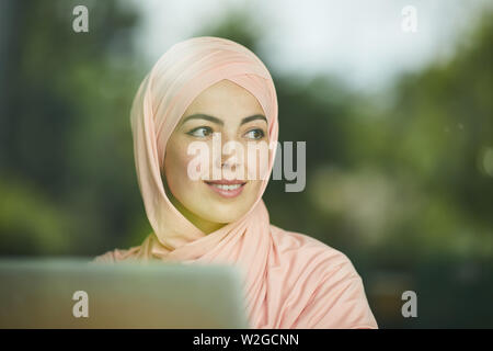Angesichts der recht junge muslimische business lady Arbeiten am Laptop und Wegsehen Stockfoto