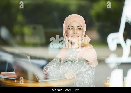 Portrait von Verträumten nachdenkliche junge muslimische Frau im Cafe sitzen, Arbeiten am Laptop und schauen durch das Fenster Stockfoto