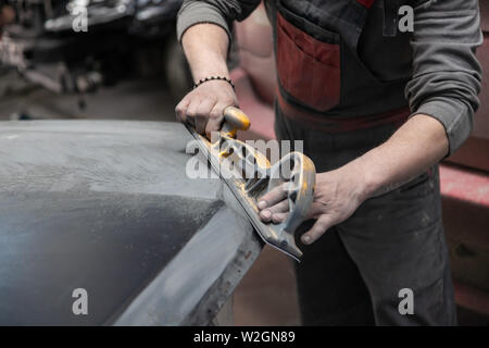 Vorbereitung für die Lackierung eines Autos mit schmirgel Absender durch einen Servicetechniker, Nivellierung, bevor Sie eine Grundierung nach der Beschädigung auf einen Teil der Stockfoto