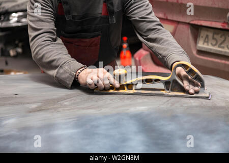 Vorbereitung für die Lackierung eines Autos mit schmirgel Absender durch einen Servicetechniker, Nivellierung, bevor Sie eine Grundierung nach der Beschädigung auf einen Teil der Stockfoto