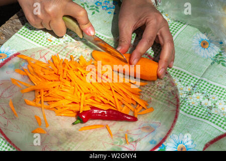 Karotten in feine Streifen schneiden und ein pod von bitter Red Pepper auf einer transparenten Schneidebrett. Stockfoto