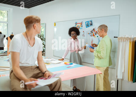 Kreative Menschen. Junge männliche Fashion Designer holding Farbmuster, während Sie seine Kollegen in einem Studio Stockfoto