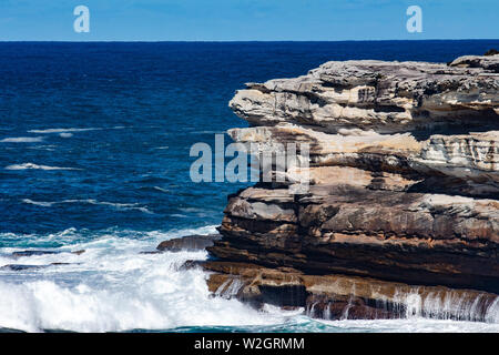 Oceanside rocky Sandsteinfelsen mit blauen Meer Wasser Wellen erzeugen Whitewash gegen Küste und klaren Himmel im Hintergrund Stockfoto