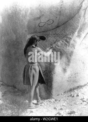 Edward S. Curtis Native American Indians - paviotso Mann stand, Kennzeichnung Seite glazialen Boulder, die bereits Petroglyphen hat es Ca. 1924 Stockfoto