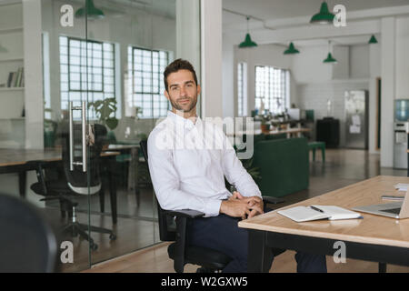 Zuversichtlich, dass junge Unternehmer an seinem Schreibtisch in einem Büro sitzen Stockfoto