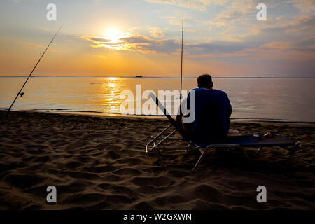 Mann sitzt auf dem Liegestuhl und Angeln vom Sandstrand, morgen über das Mittelmeer. Stockfoto
