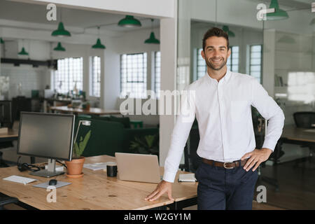 Lächelnde junge Unternehmer lehnte sich gegen eine Tabelle in einem Büro Stockfoto