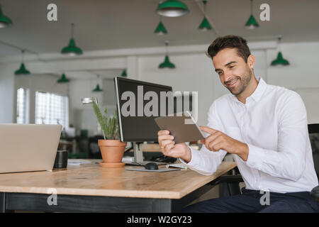 Lächelnd Geschäftsmann an seinem Schreibtisch sitzend mit einem digitalen Tablet Stockfoto