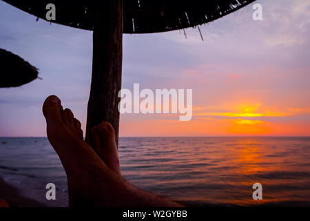 Man Beine bis zum Sonnenbaden ist liegend sorglos in Liege neben der Küste, am öffentlichen Strand. Stockfoto