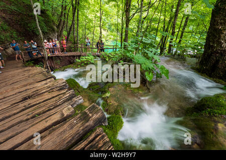 Wanderer entlang der Holzsteg, Kaskaden von Wasser, hetzen die Felsen am Nationalpark Plitvicer Seen, Kroatien bummeln Stockfoto