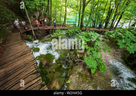 Wanderer entlang der Holzsteg, Kaskaden von Wasser, hetzen die Felsen am Nationalpark Plitvicer Seen, Kroatien bummeln Stockfoto