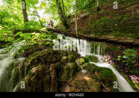 Wanderer entlang der Holzsteg, Kaskaden von Wasser, hetzen die Felsen am Nationalpark Plitvicer Seen, Kroatien bummeln Stockfoto