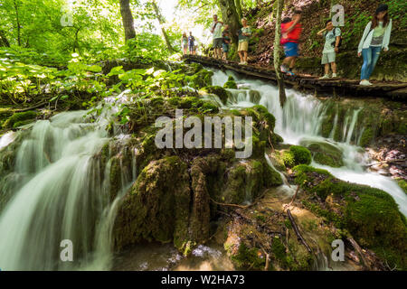 Wanderer entlang der Holzsteg, Kaskaden von Wasser, hetzen die Felsen am Nationalpark Plitvicer Seen, Kroatien bummeln Stockfoto