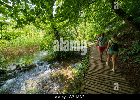 Wanderer entlang der Holzsteg, Kaskaden von Wasser in Richtung versteckte Teiche an den Nationalpark Plitvicer Seen, Kroatien hetzen Bummeln Stockfoto