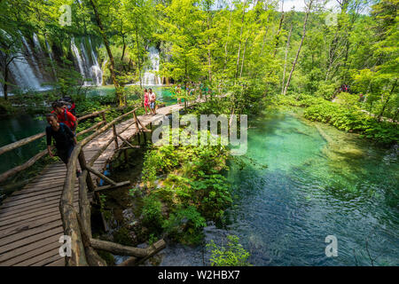 Wanderer entlang der Holzsteg, Kaskaden von Wasser in türkisfarbenen Teiche an den Nationalpark Plitvicer Seen hetzen Bummeln Stockfoto