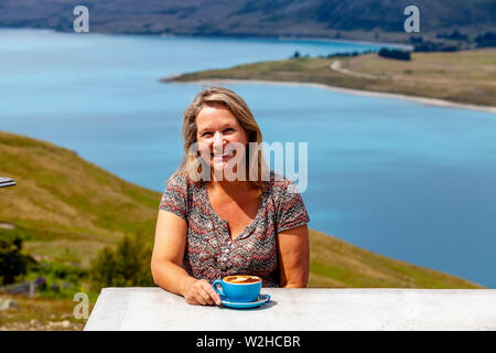 Eine Frau mittleren Alters saß bei einer Tasse Kaffee mit Blick auf den See Tekapo, Mt John Observatorium Viewpoint, Mackenzie District, South Island, Neuseeland Stockfoto