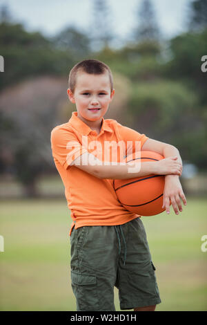 Ein Porträt der jungen kaukasischen Jungen legere Kleidung, hält er einen Basketball und ein Blick auf die Kamera. Stockfoto