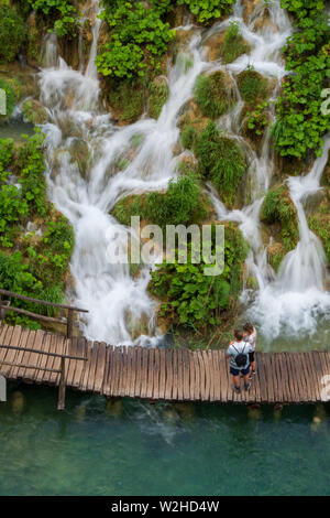 Wanderer ein Spaziergang entlang der Holzsteg, Kaskaden von Wasser, ausgegossen in die azurblauen See Kaluđerovac an den Plitvicer Seen Nationa Stockfoto